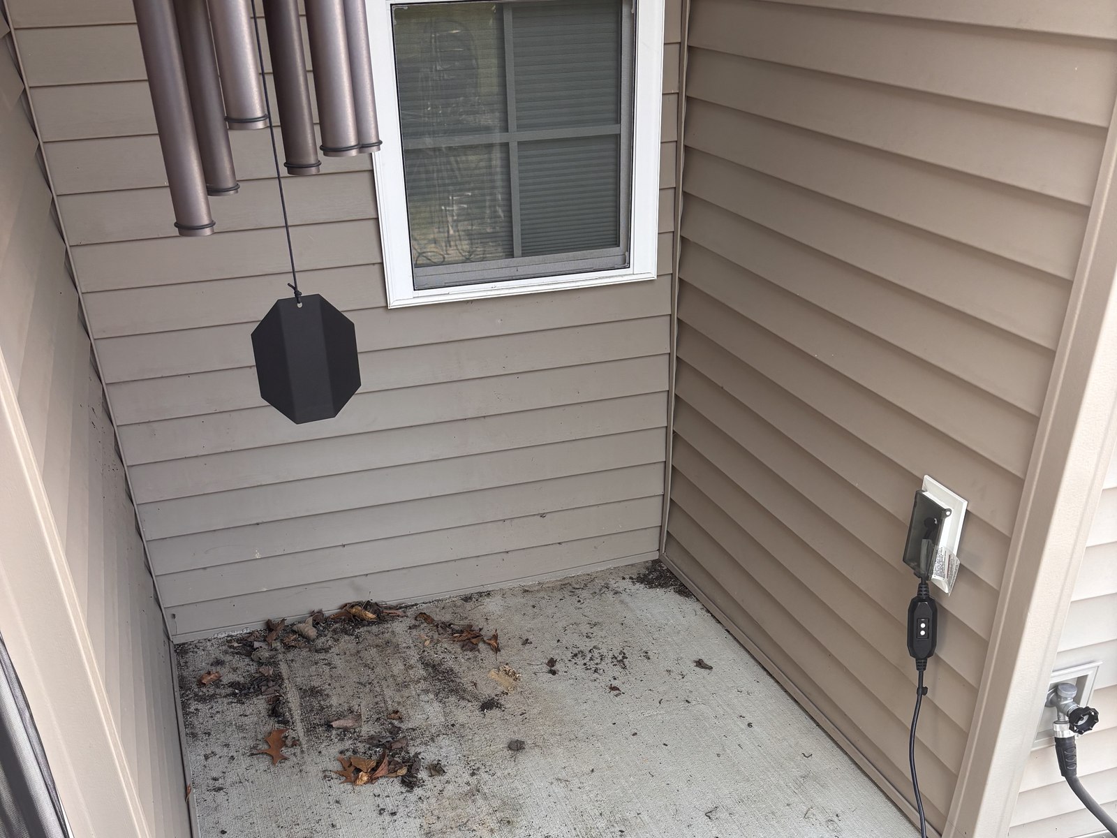 A covered porch before cleaning, with leaves, dirt and dark staining across the concrete floor
