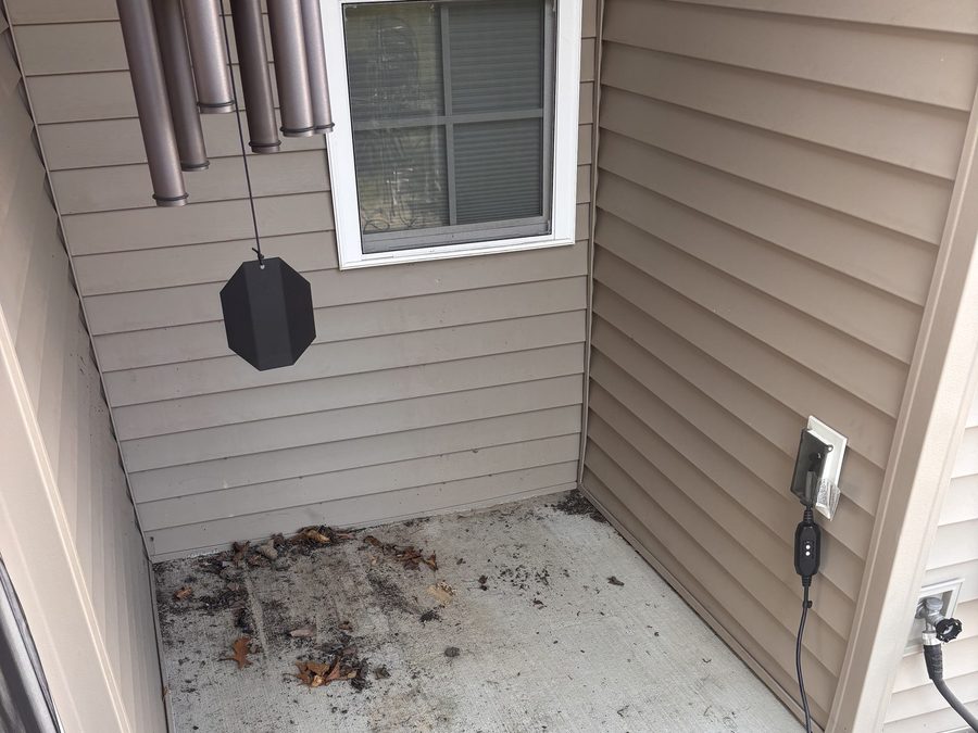 A covered porch before cleaning, with leaves, dirt and dark staining across the concrete floor