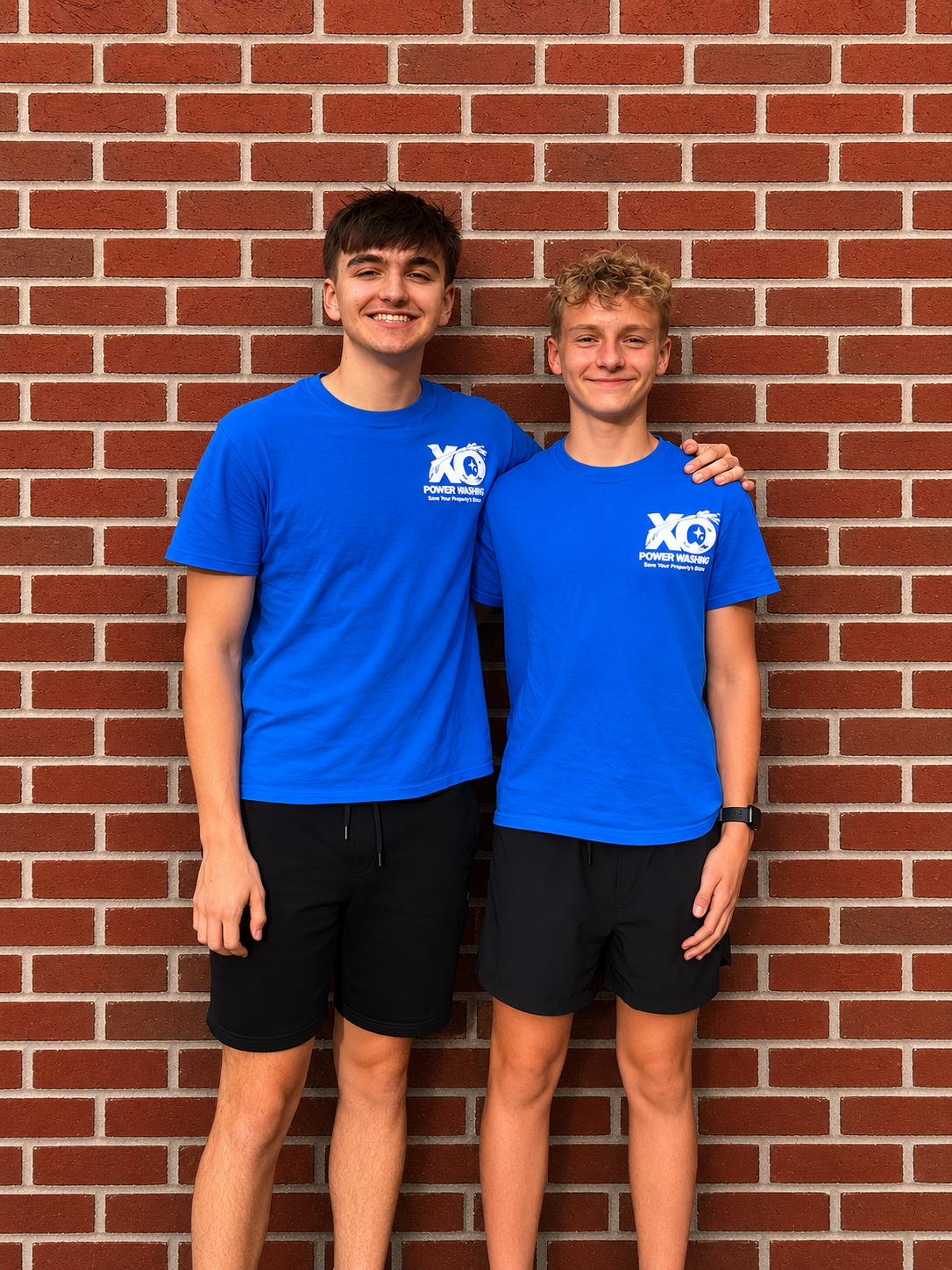 The two founders of XO Power Washing in branded shirts in front of a brick wall
