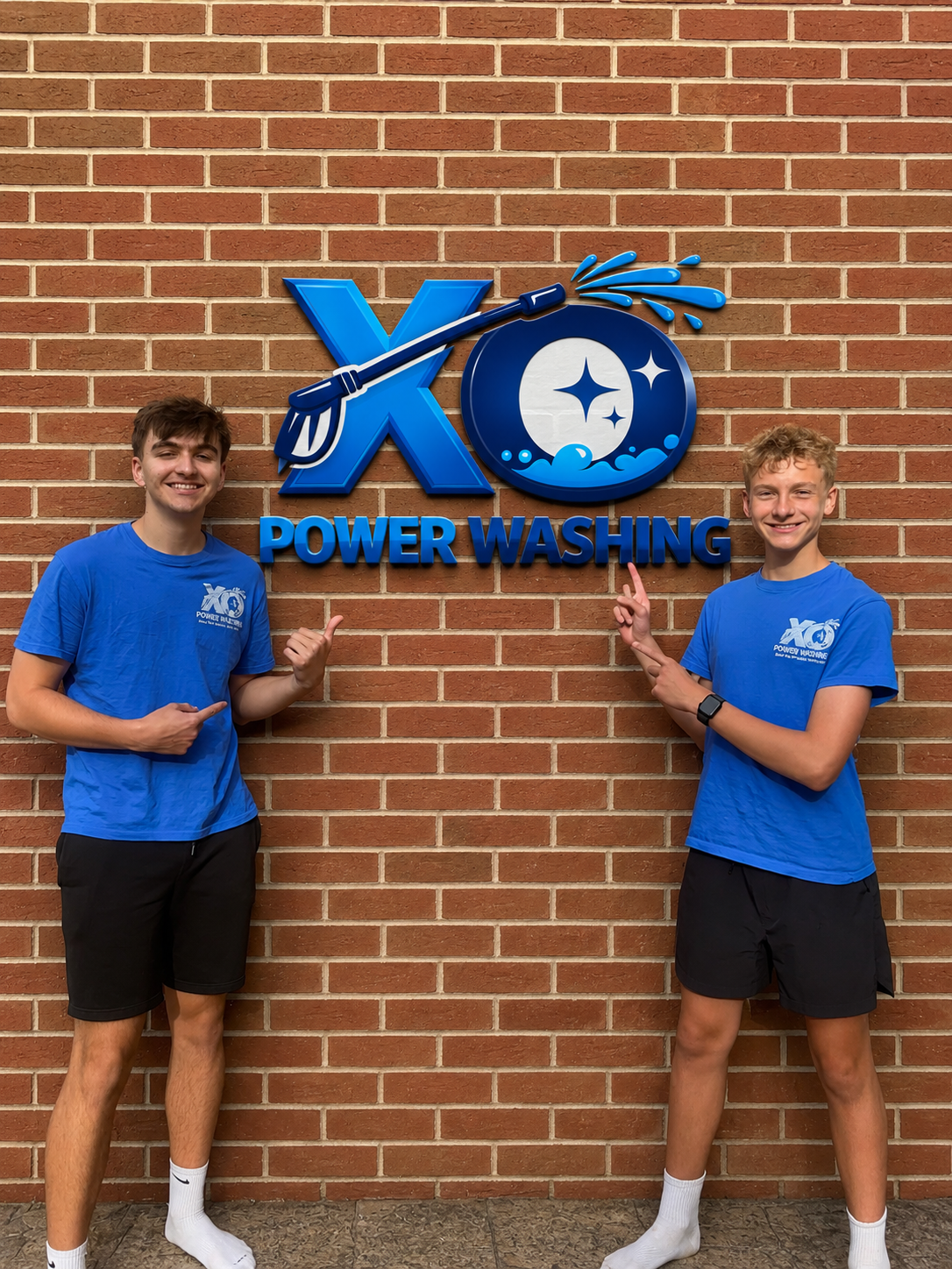 The XO Power Washing founders pointing at the XO Power Washing logo sign